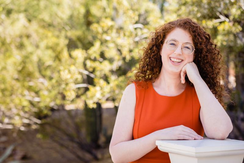 A redheaded woman in an orange dress smiling