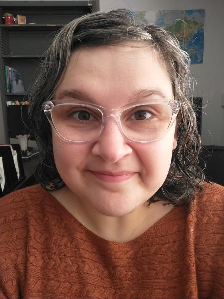 a photo of a woman with brown and gray hair, clear glasses, and a brown sweater