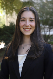 Smiling girl with long brown hair, trees in background