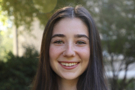 Smiling girl with long brown hair, trees in background